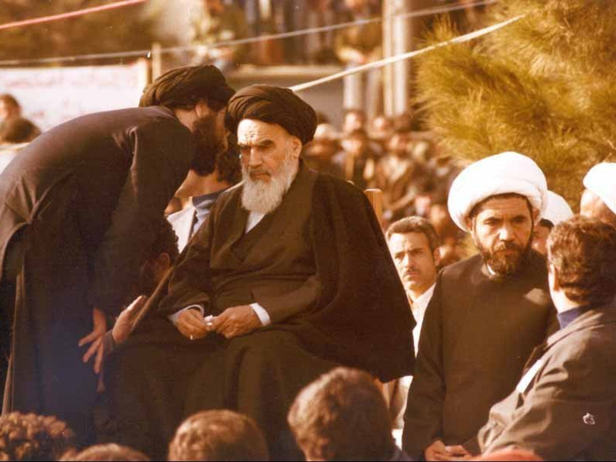 photo of a young cleric talking into the ear of the Ayatollah
