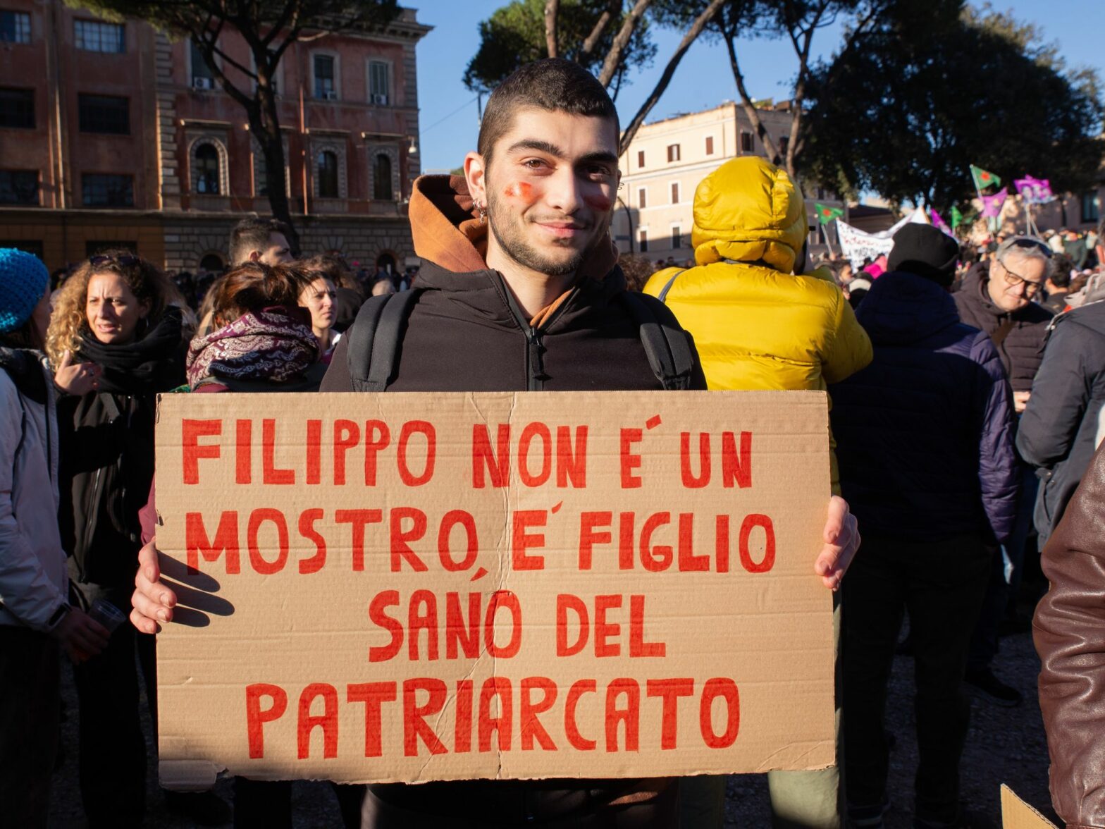 photo of a young man holding a sign: Filippo isn't a monster, he's the healthy son of the patriarchy