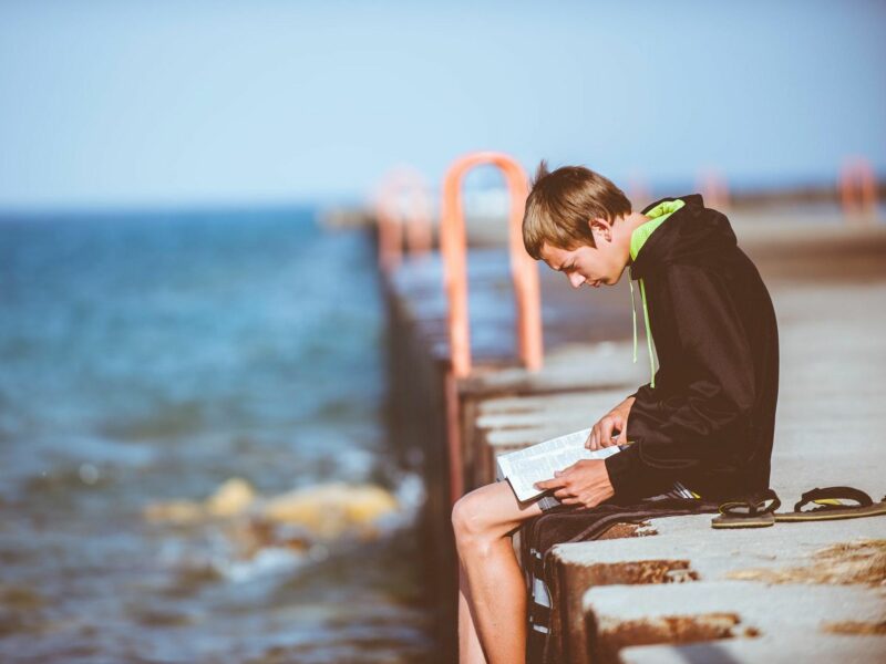 photo of a young man on a dock reading