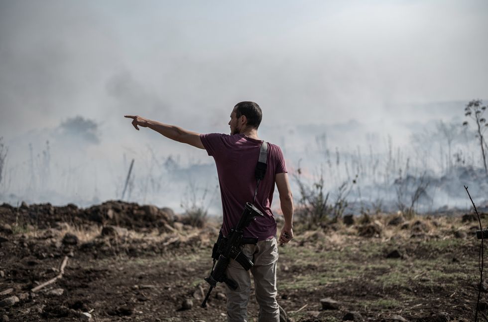 Photo of an armed man standing on a field, surrounded by smoke, in Katsrin, in Israel's Golan Heights, after a strike from Lebanon into Israel on June 13
