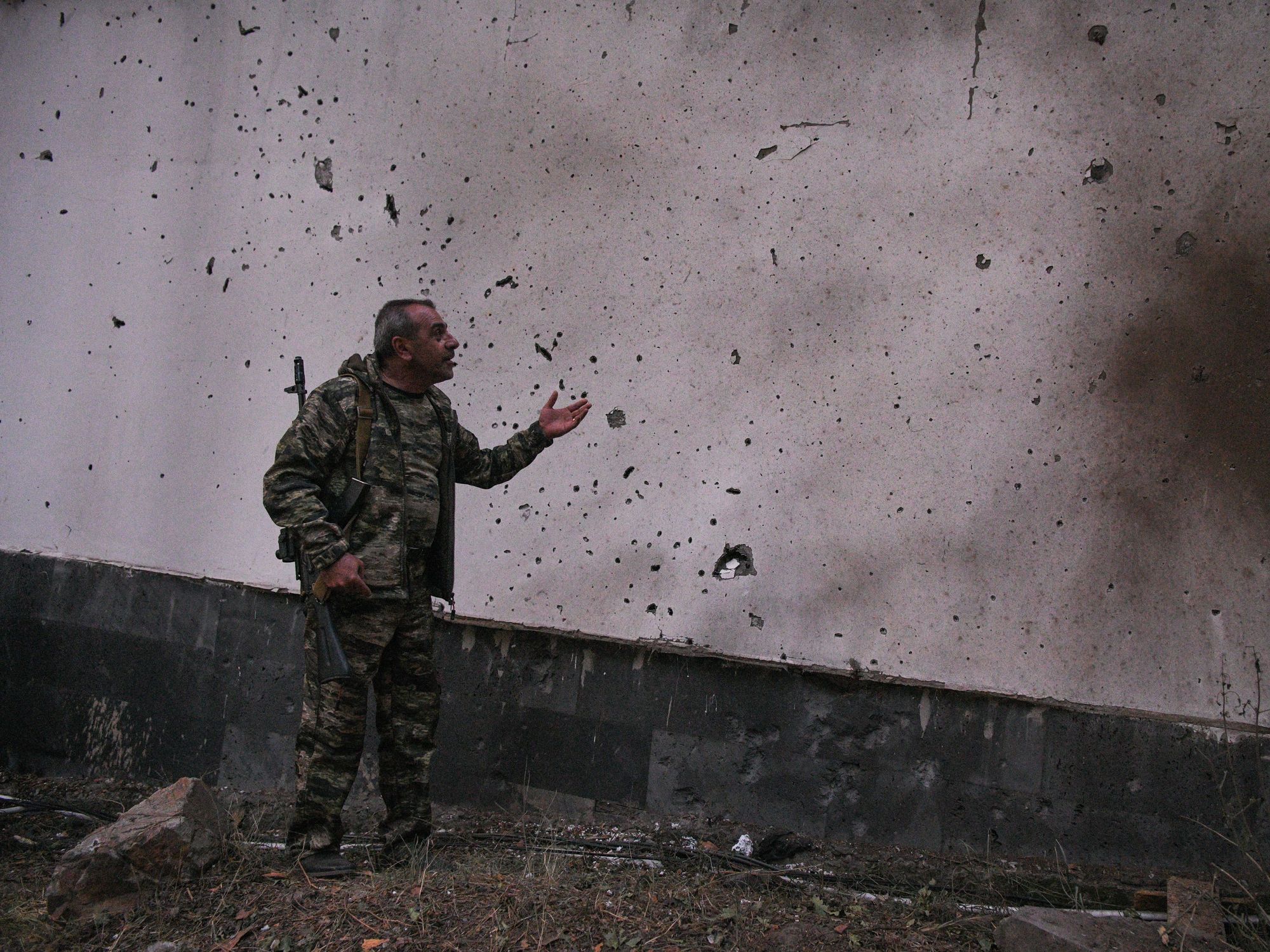 photo of an Armenian soldier looking at a damaged wall.