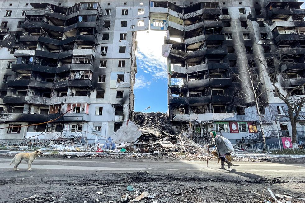 Photo of an elderly woman with her dogs walking past a damaged residential building by a Russian airstrike in Borodyanka, Ukraine.