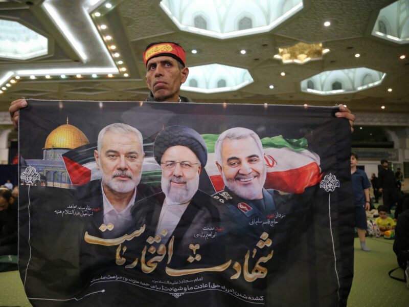 Photo of An Iranian man holds a flag showing late Ismail Haniyeh, late Iranian President Ebrahim Raisi and former Iranian major general Qasem Soleimani.