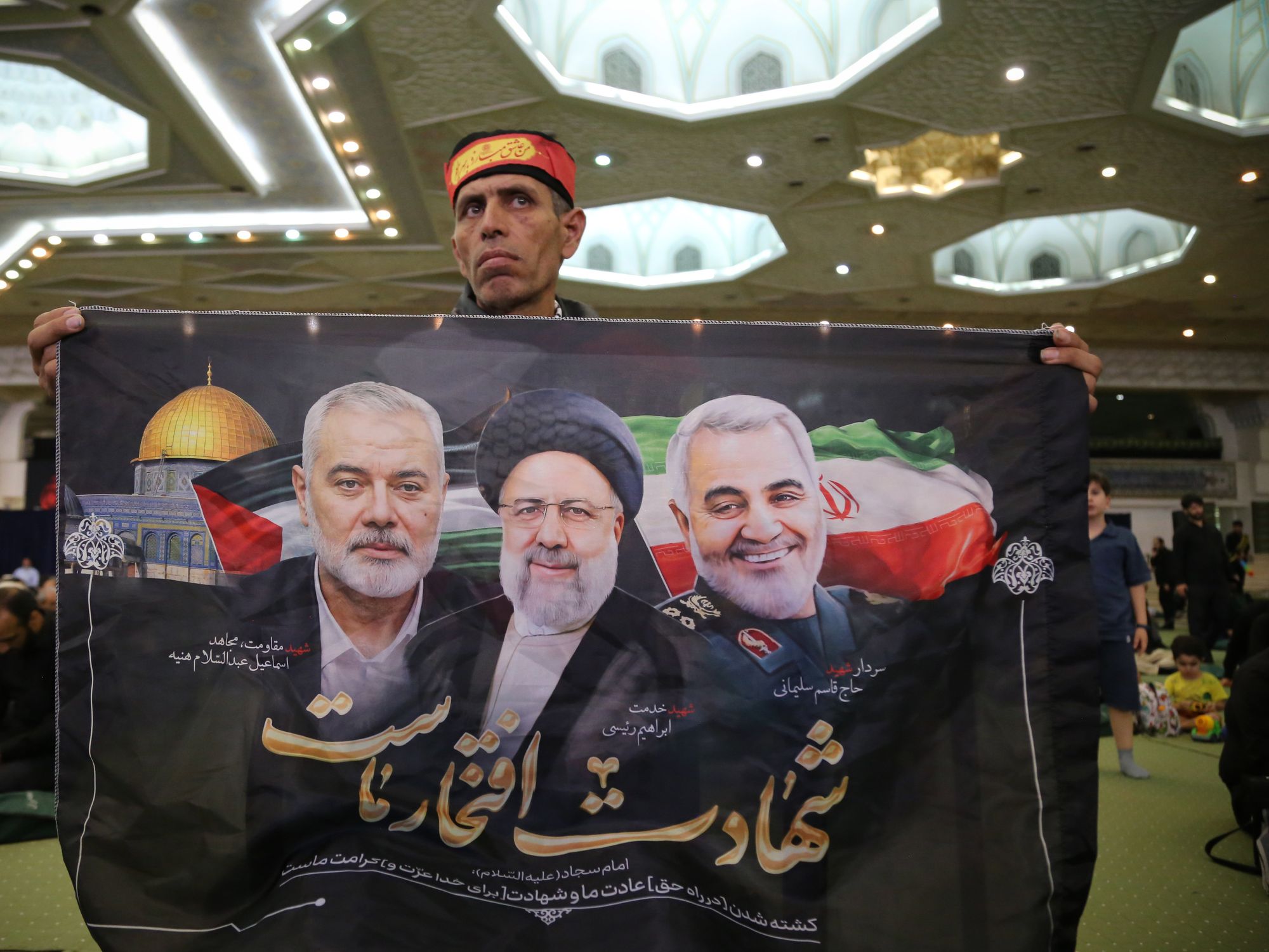 Photo of An Iranian man holds a flag showing late Ismail Haniyeh, late Iranian President Ebrahim Raisi and former Iranian major general Qasem Soleimani.