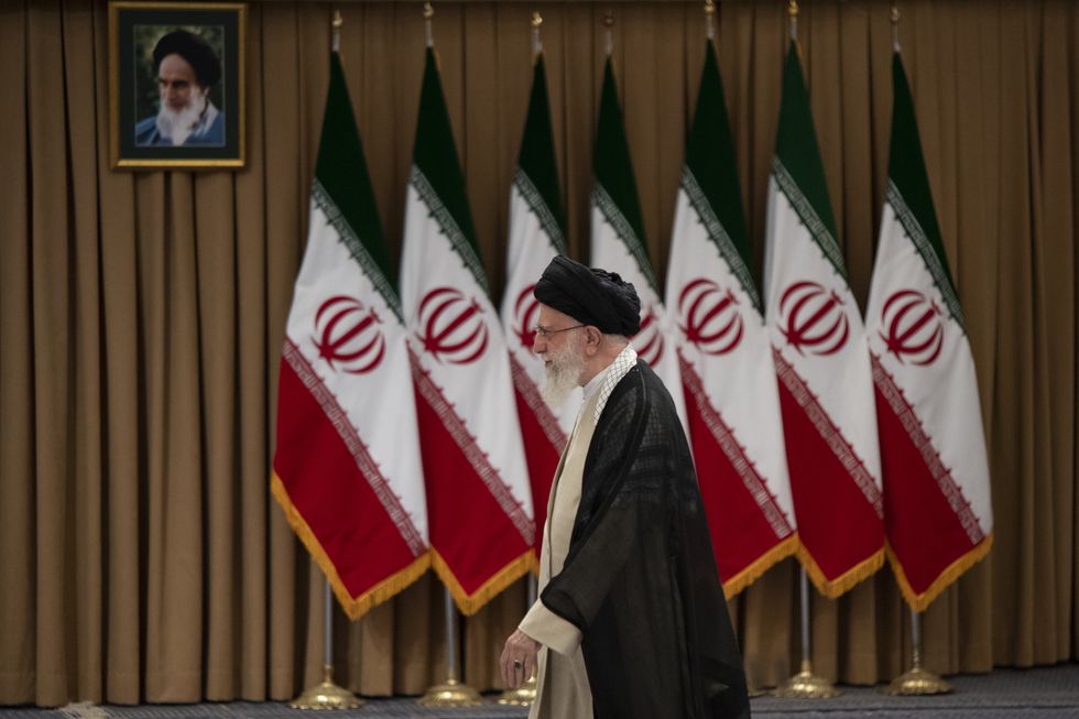 Photo of an Iranien official walking past curtains, seven flagpoles and a picture of anothe rofficial.