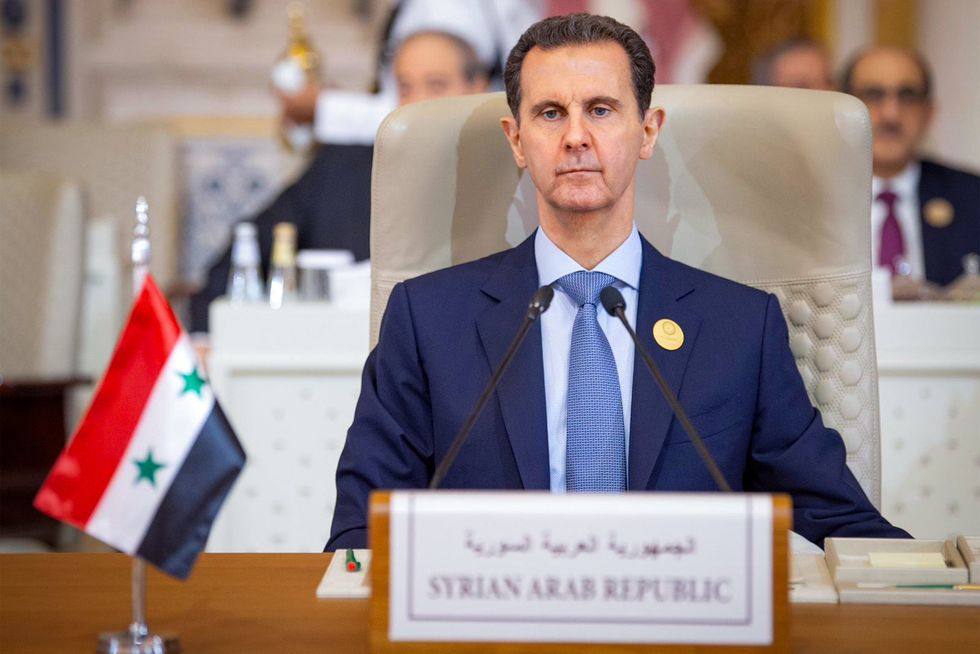 photo of Assad at a table with a small Syrian flag