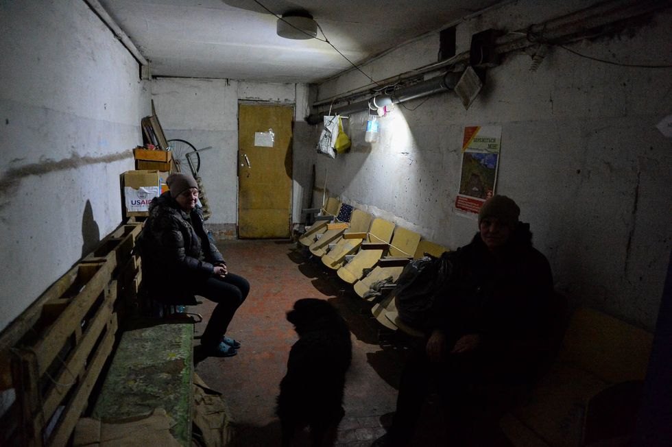 Photo of Avdiivka residents, Luba and Mayoarva, sitting with their dog as cluster munitions land above.