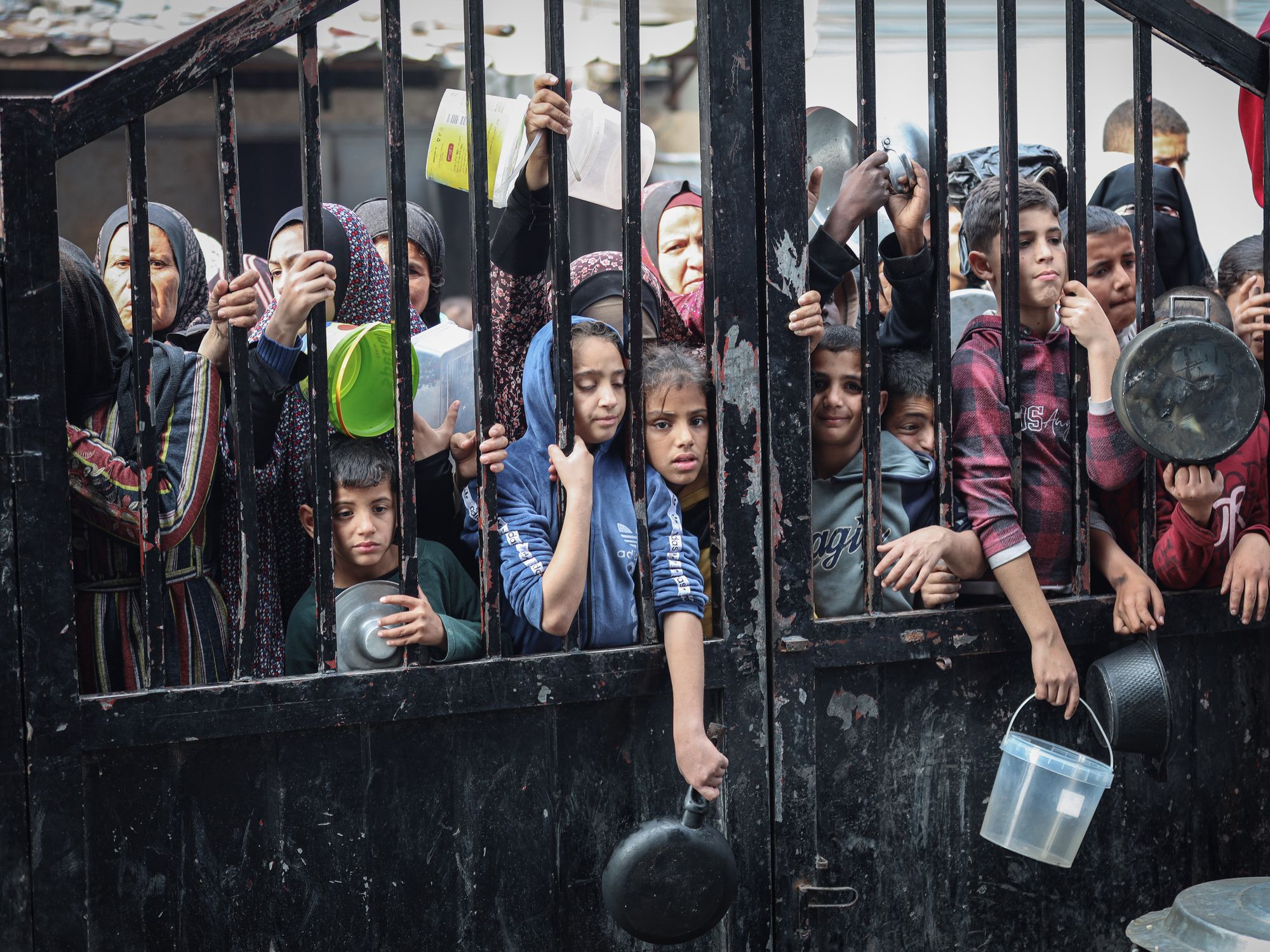 photo of children lined up at a gate with pots, pans, buckets