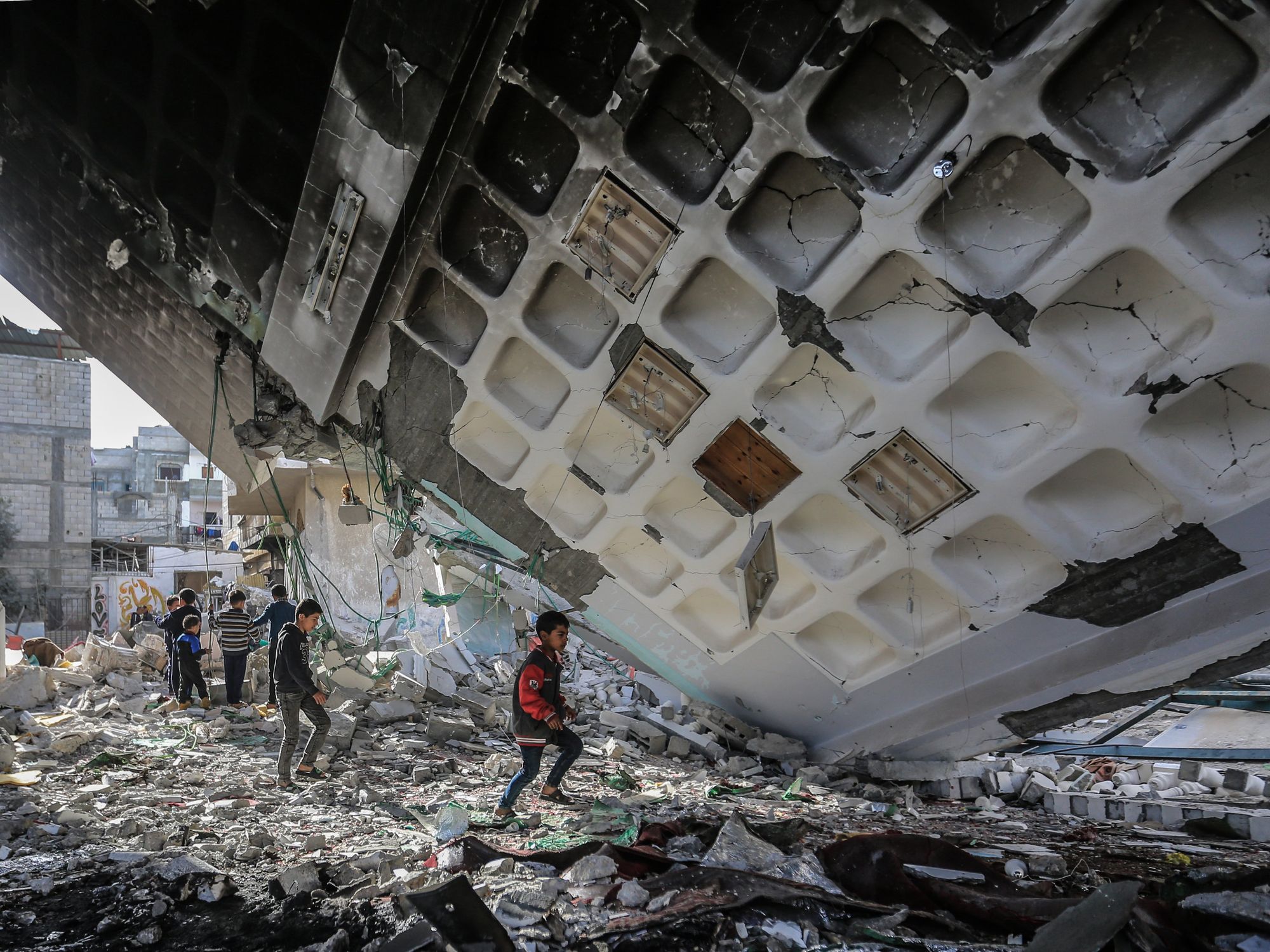 Photo of children walking under the remains of Al-Huda Mosque destroyed in an Israeli bombing