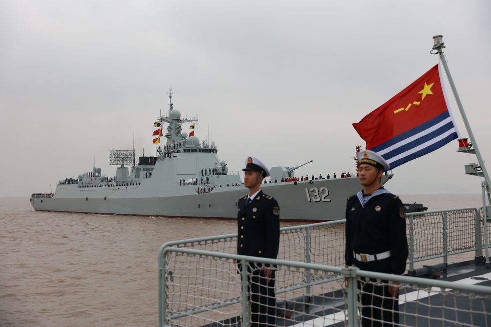 photo of chinese naval personnel standing at attention with a missile destroyer behind them