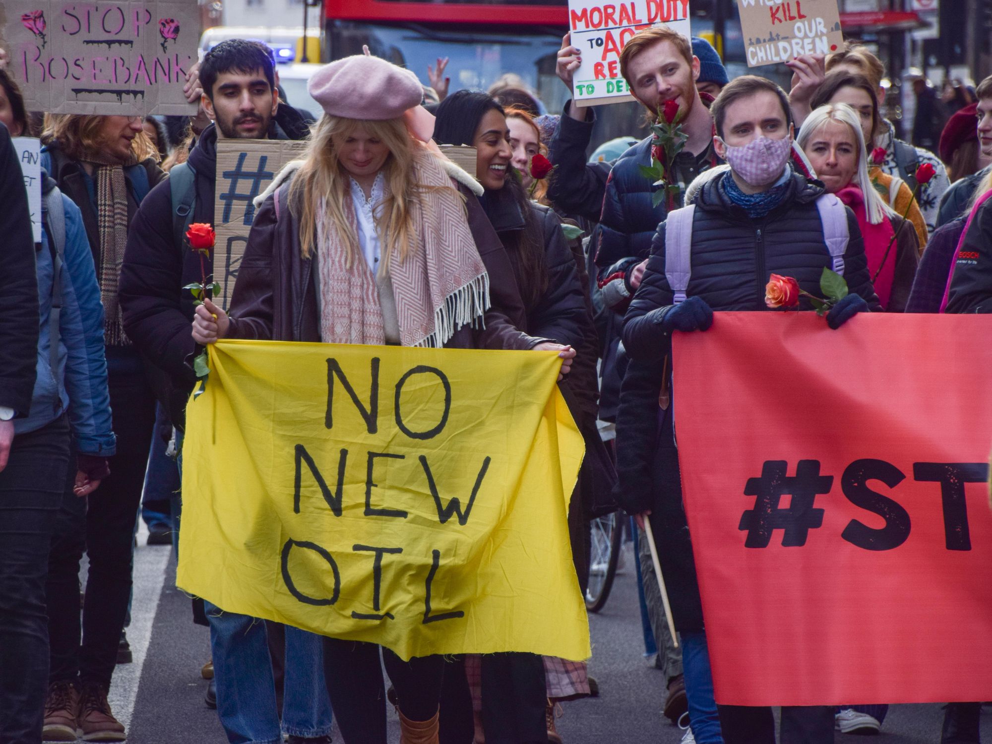 photo of climate activist holding a yellow sign that says No New Oil