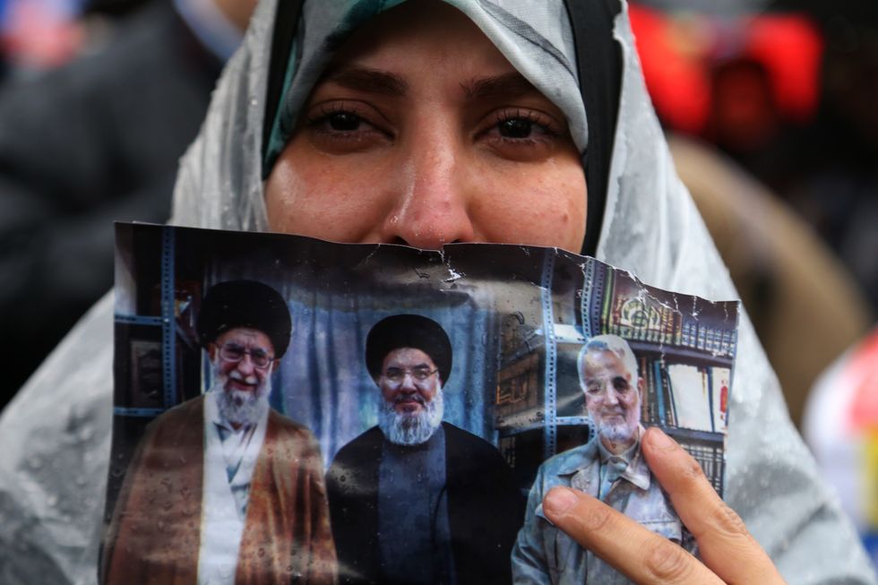 photo of ​A woman holding a picture of Khamenei, Nasrallah and Soleimani