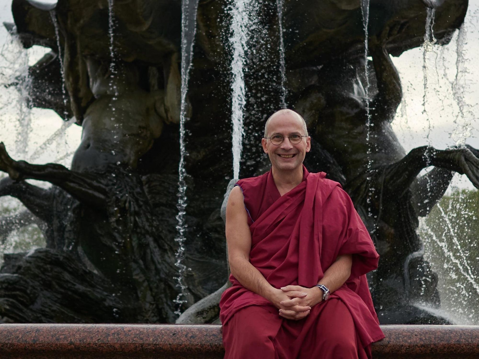 Photo of ​Berlin-born Buddhist monk ​Tenzin Peljor sitting near a fountain