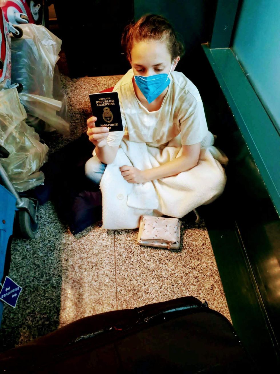 Photo of ​Milagros Almeida showing her Argentine passport while sitting on the floor at Madrid's Barajas airport