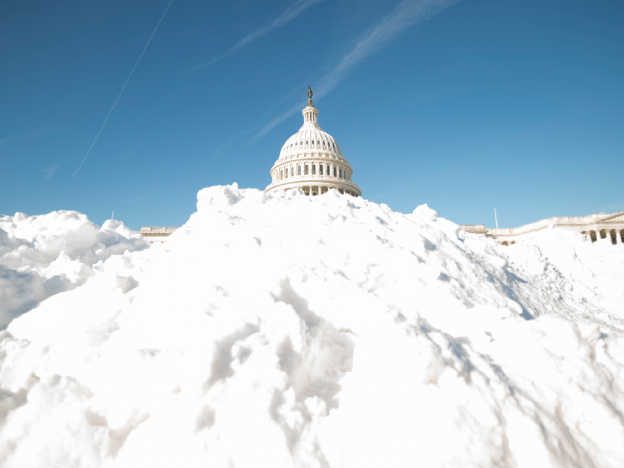 Photo of ​the U.S. Capitol dome emerging from a mound of snow (thanks to a perspective trick) as Washington, D.C. receives its first blizzard in years.