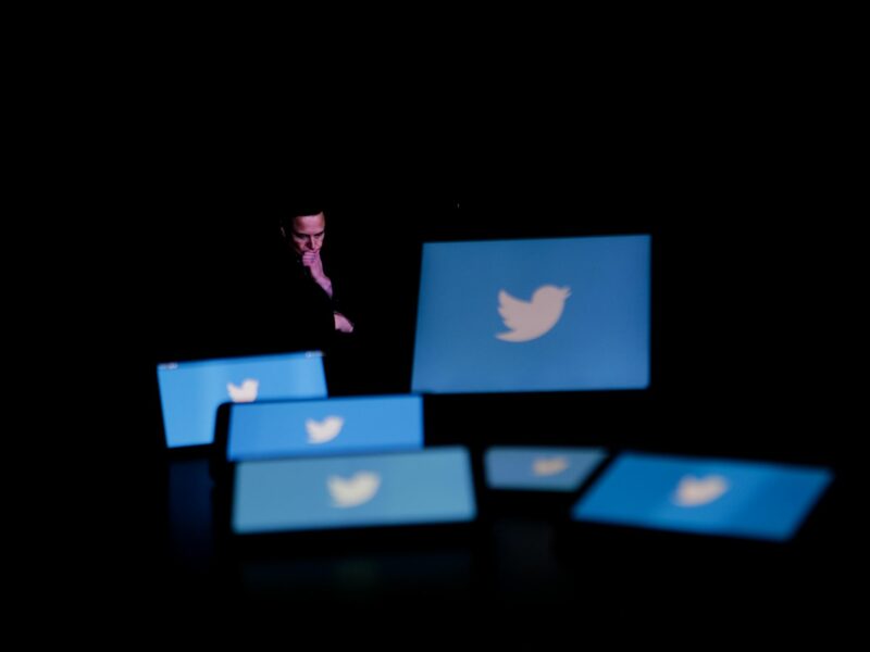 Photo of Elon Musk looking down at screens featuring Twitter's blue bird logo