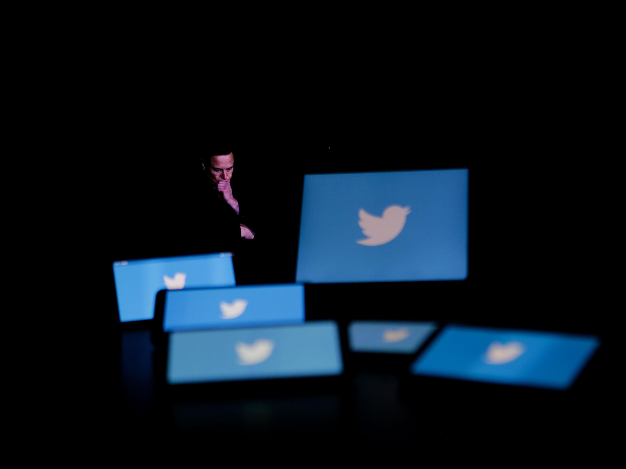 Photo of Elon Musk looking down at screens featuring Twitter's blue bird logo