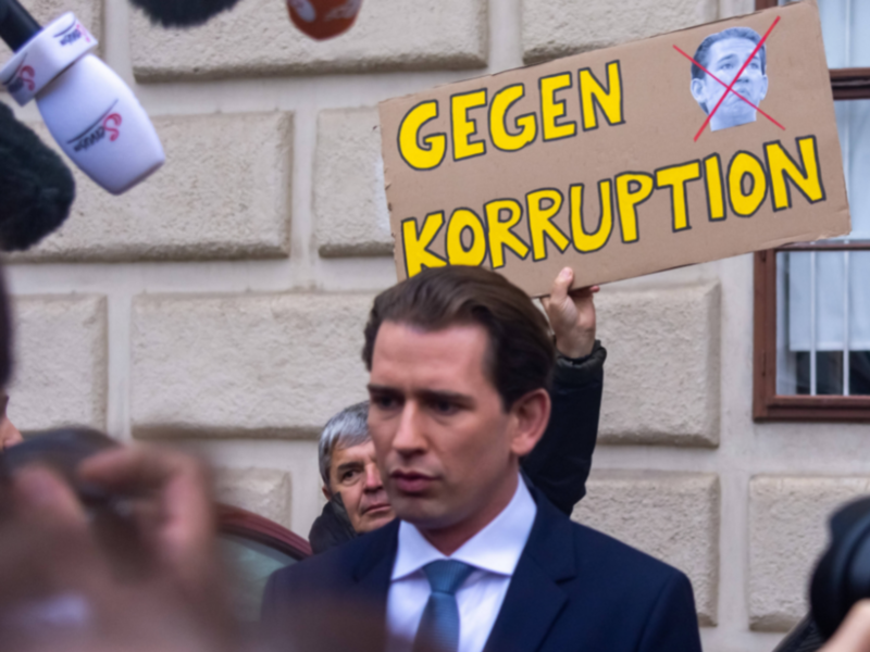 Photo of former Austrian Chancellor Sebastian Kurz in front of a protestor holding a placard that read "Against corruption" in Austrian
