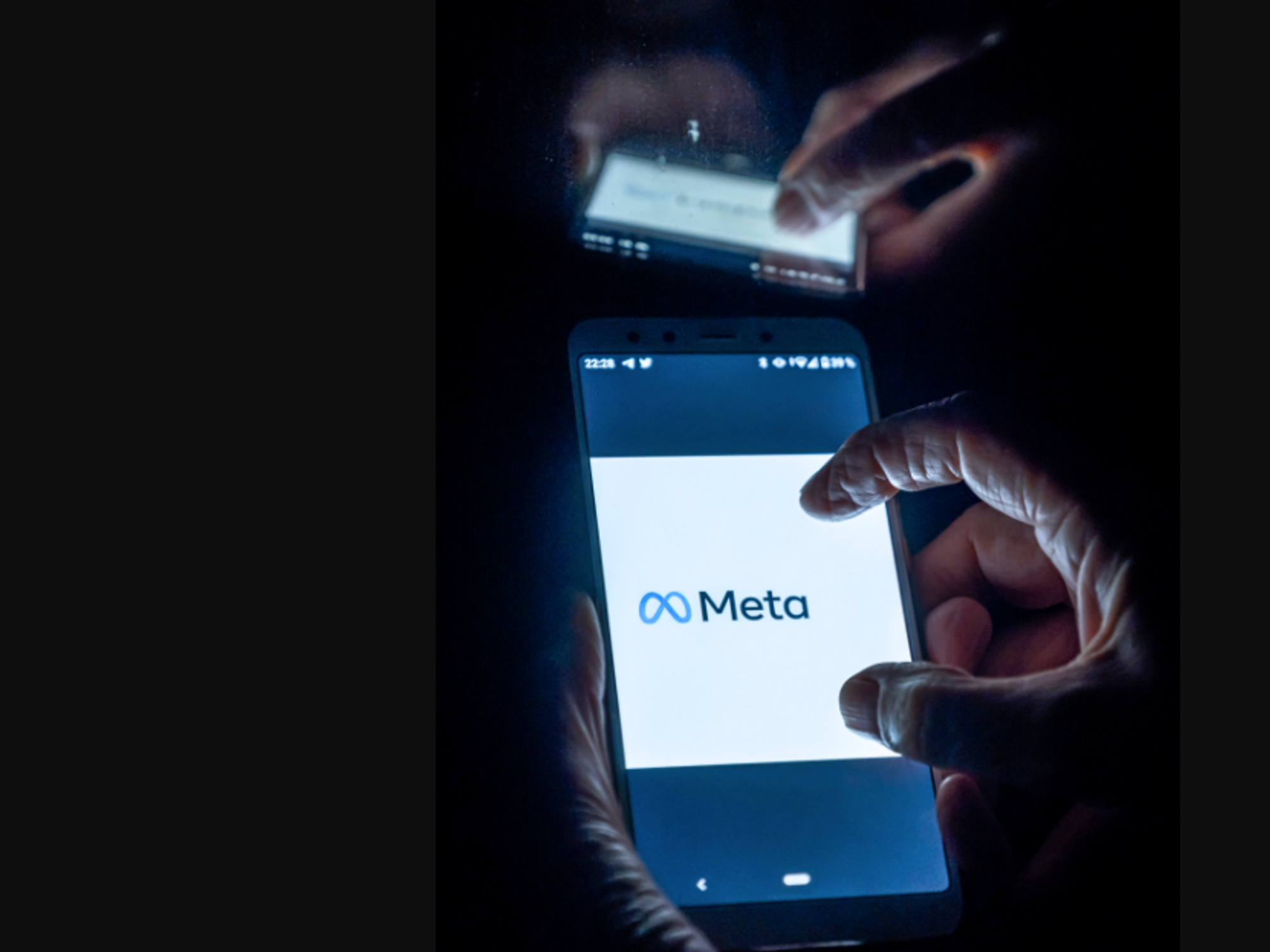 Photo of hands zooming in on a phone screen that displays the logo and name of Facebook's new name, Meta.