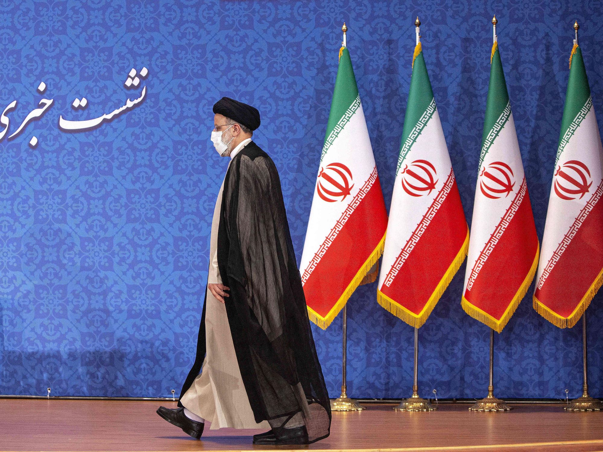 Photo of Iran's President Ebrahim Raisi walking on a stage in front of Iranian flags