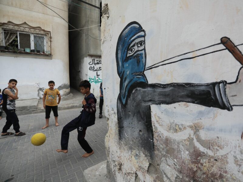 photo of kids playing soccer with a mural of someone shooting a slingshot
