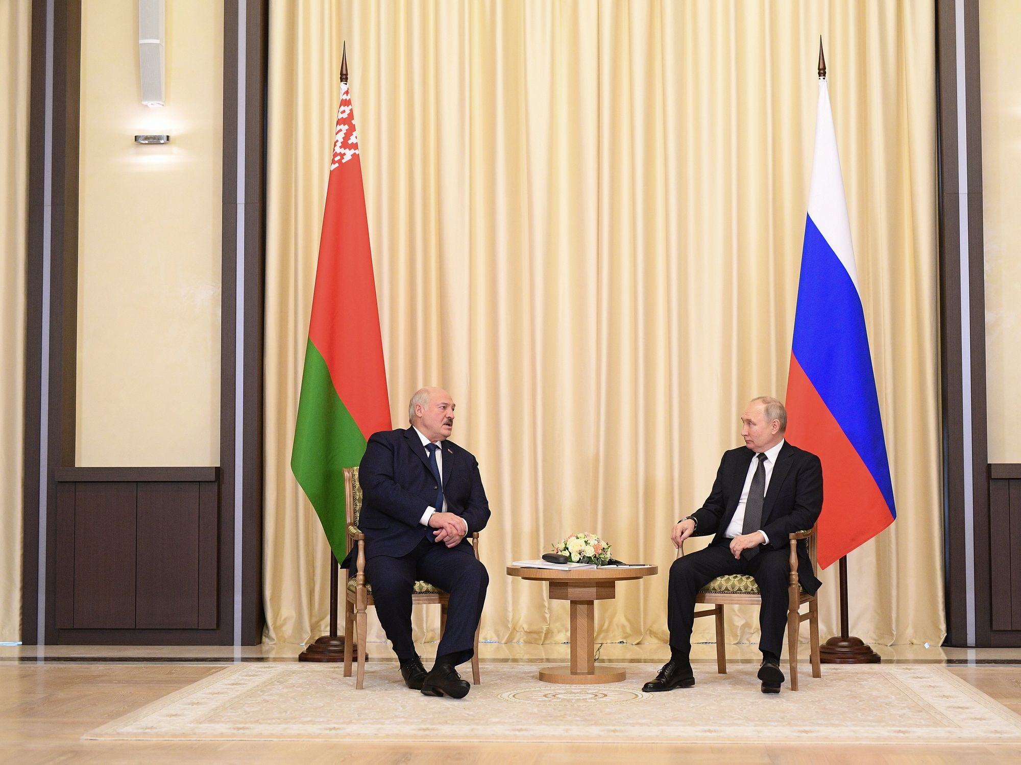 photo of lukashenko and putin sitting on chairs in front of their national flags