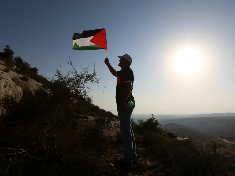 photo of man holding palestinian flag on a mountain top