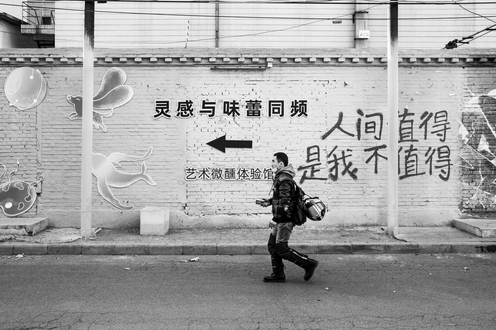 photo of man walking with chinese writing and an arrow on the wall