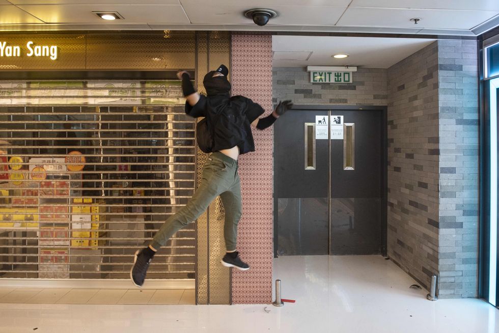 photo of masked protester jumping up to smash a surveillance camera