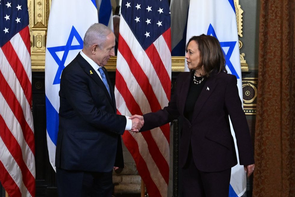 photo of netanyahu and harris shaking in hands in front of israeli and american flags.
