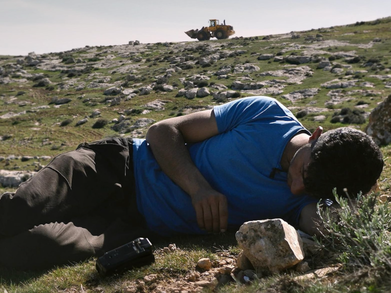 Photo of Palestinian activist Basel Adra lying on a rock-studded hill, his handheld camera on the ground nearby.