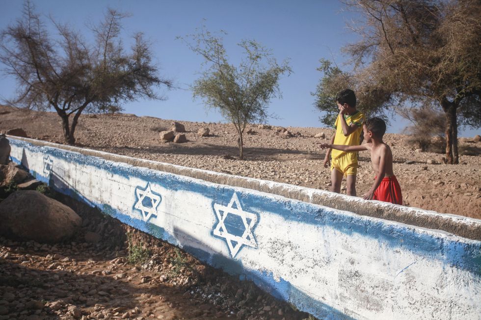 Photo of Palestinian children stand next to a channel of the Uja River canal with an Israeli flag painted on it.