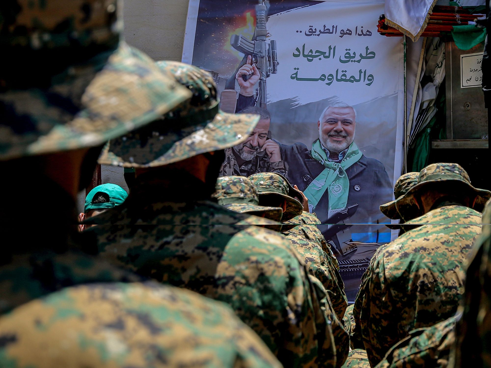 Photo of Palestinian Hamas militants sitting in front of a poster of the group's slain leader Ismail Haniyeh