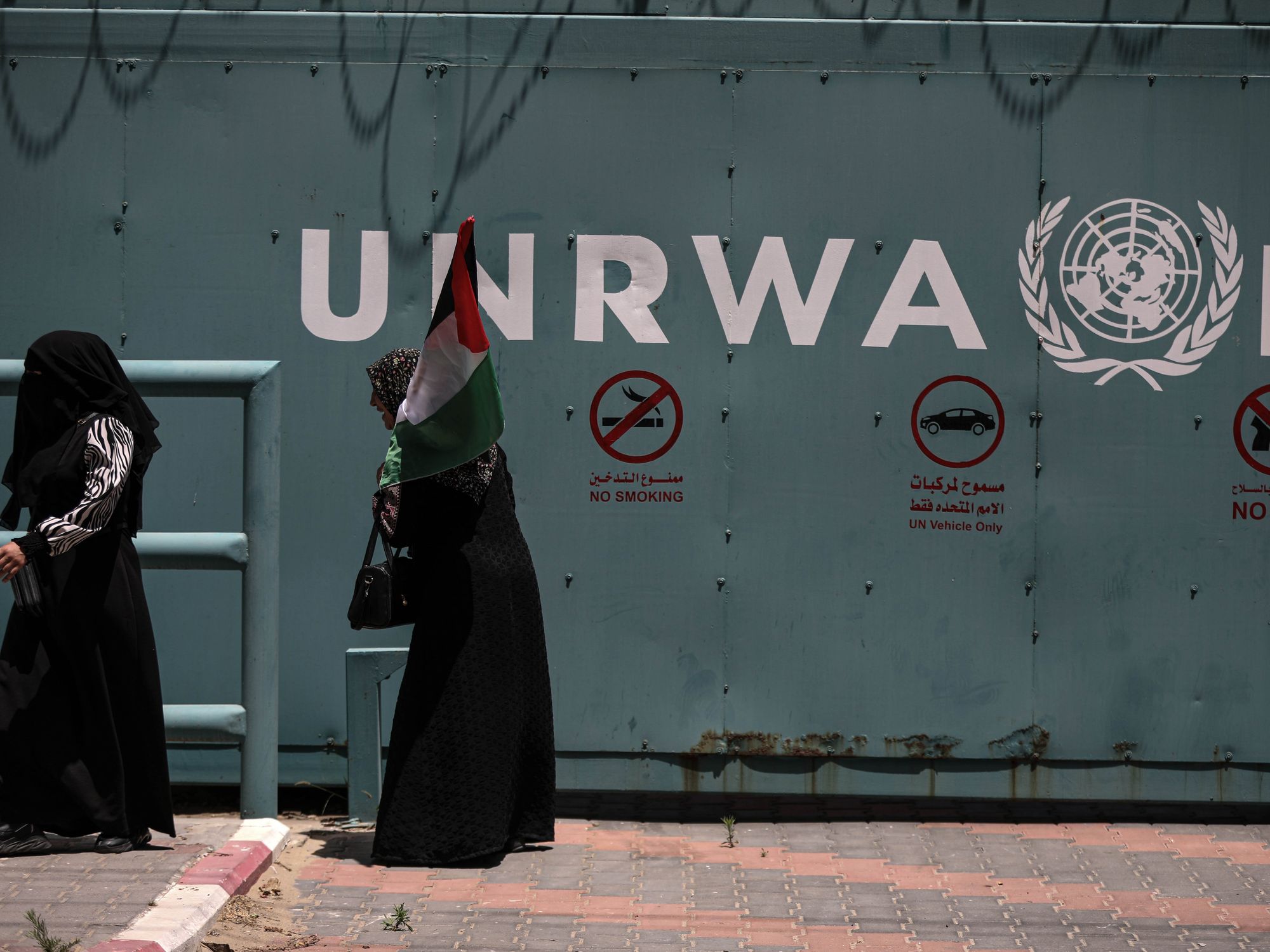 Photo of Palestinian women walking by the UNRWA headquarters in Gaza City, carrying a Palestinian flag