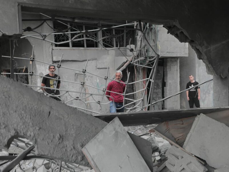 Photo of Palestinians standing among the rubble, inspecting the damage