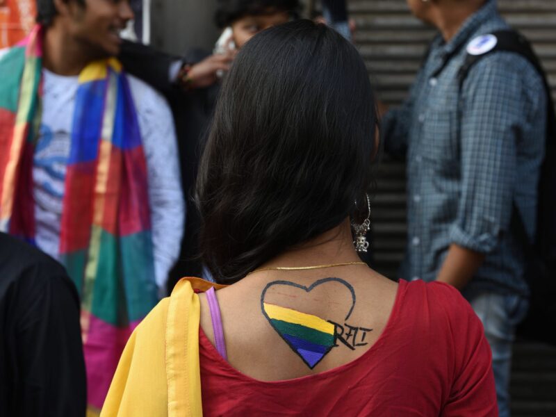 Photo of participants of a Pride March in Kolkata, India, standing in front of a colorful mural