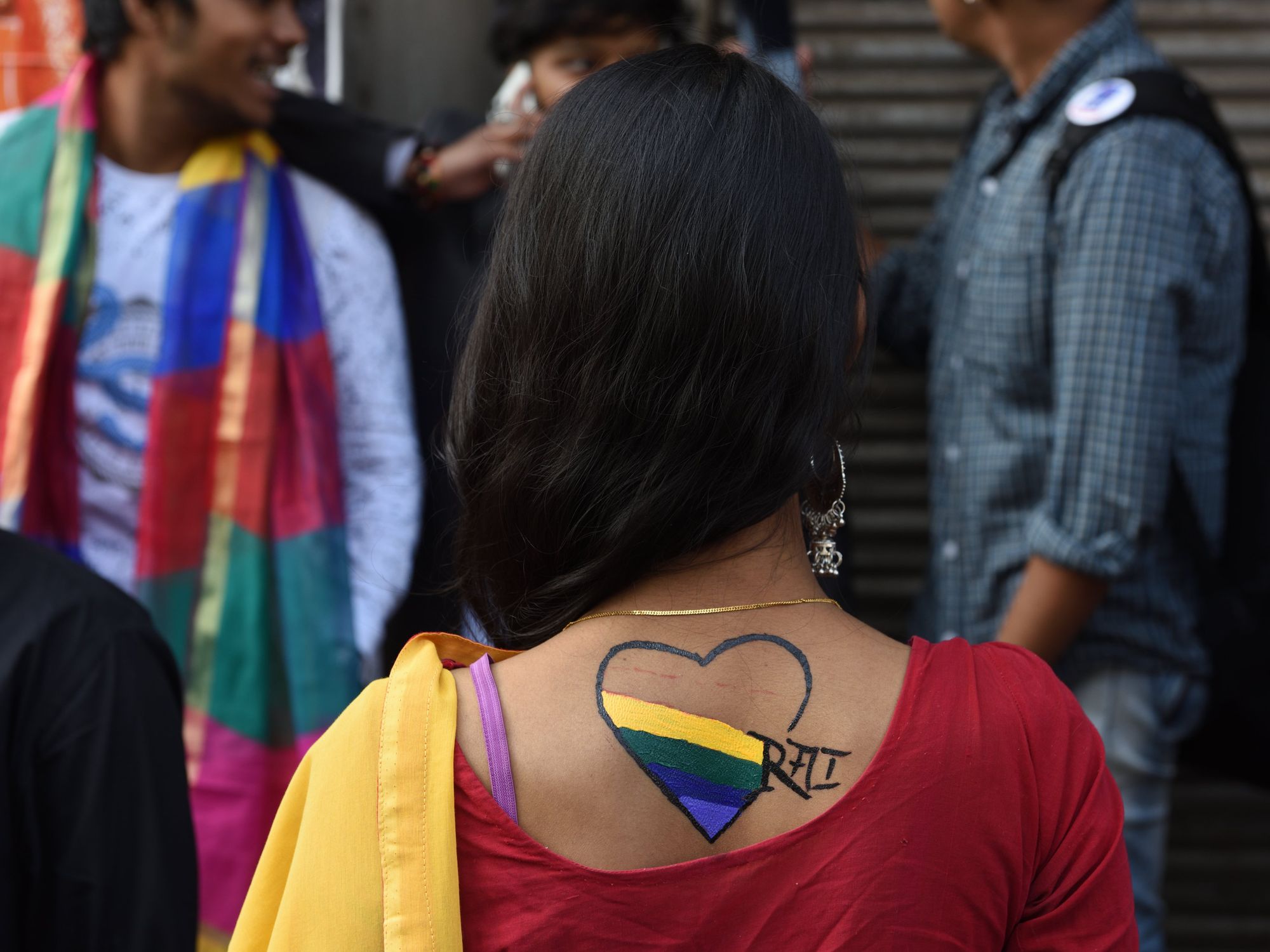 Photo of participants of a Pride March in Kolkata, India, standing in front of a colorful mural