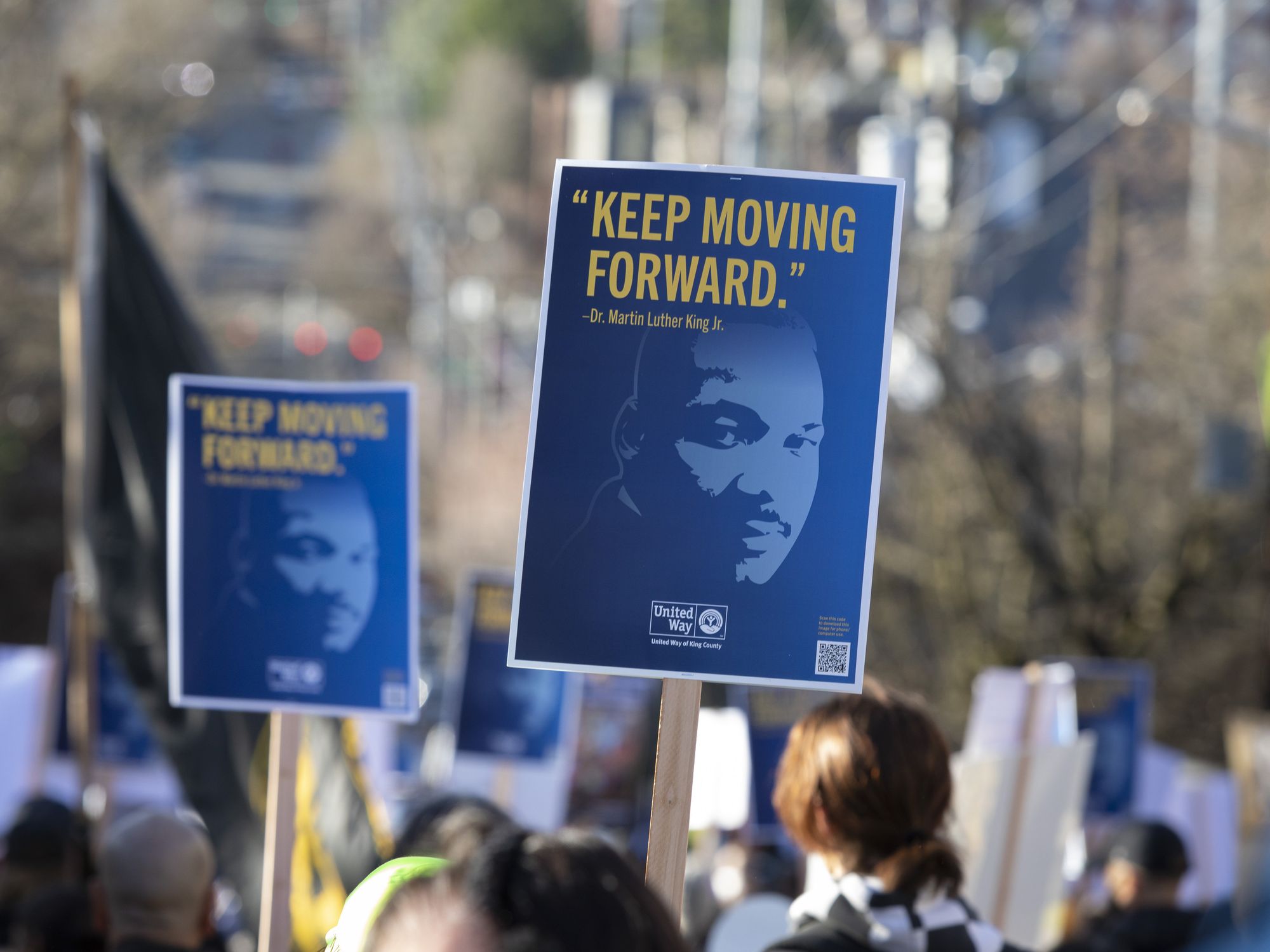 Photo of people holding up signs with MLK's face, reading "Keep moving forward".