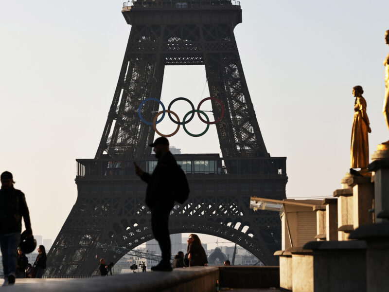 Photo of people in front of the Eiffel Tower, with the Olympic rings installed mid-height