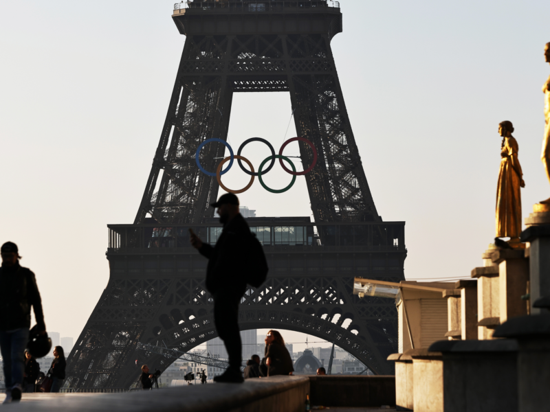 Photo of people in front of the Eiffel Tower, with the Olympic rings installed mid-height