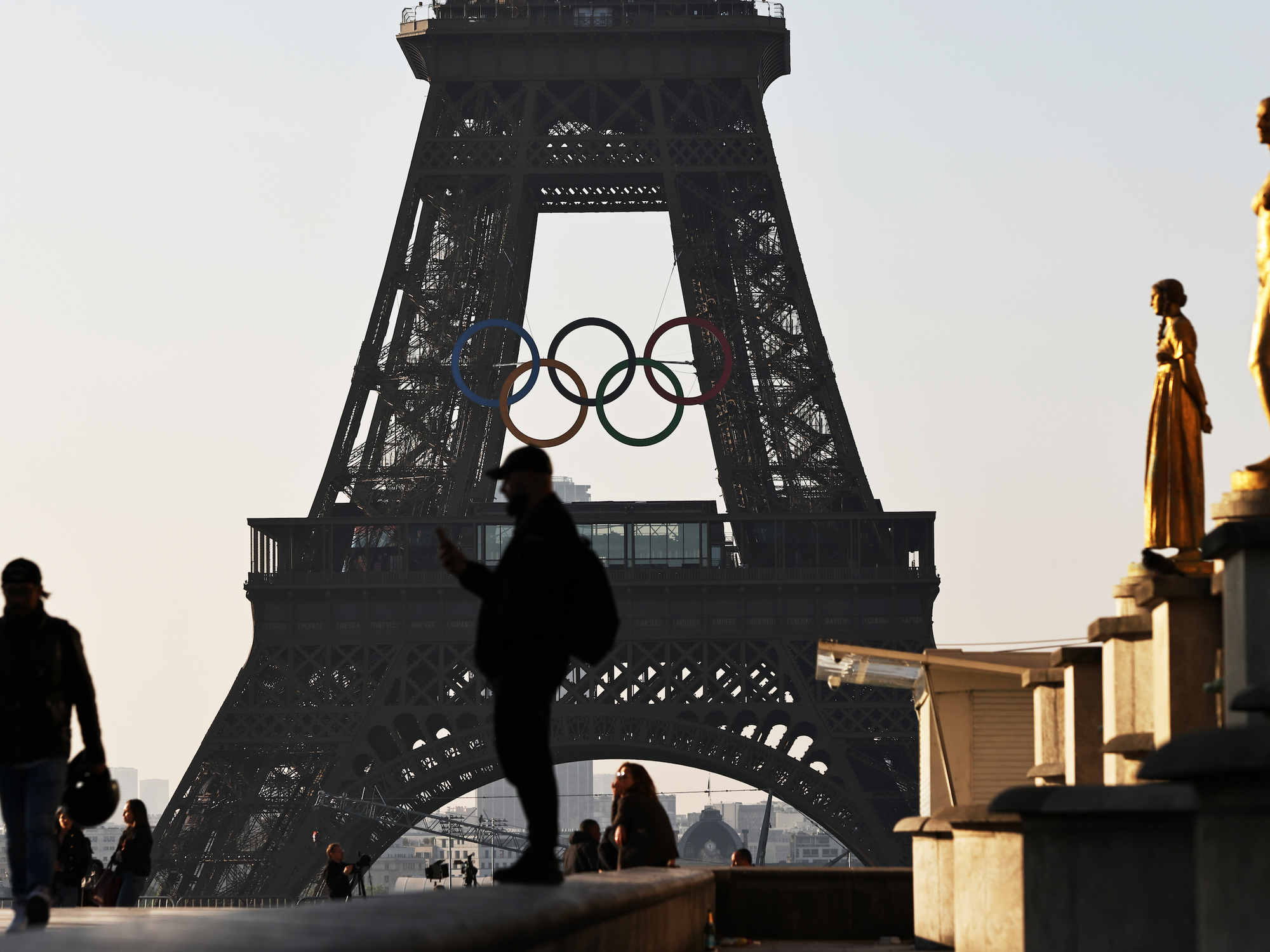 Photo of people in front of the Eiffel Tower, with the Olympic rings installed mid-height