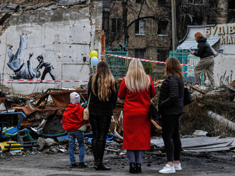 photo of people looking at a destroyed building with a wall containing a Banksy work