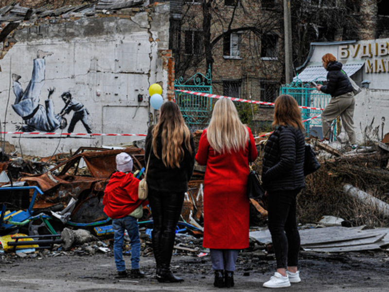 photo of people looking at a destroyed building with a wall containing a Banksy work