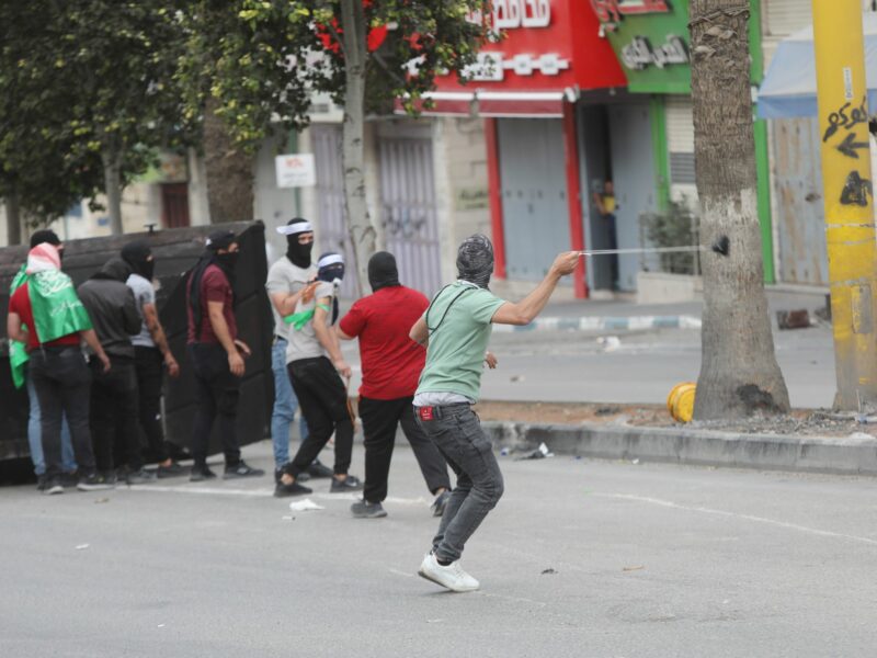 Photo of people Palestinians throwing stones toward Israeli troops