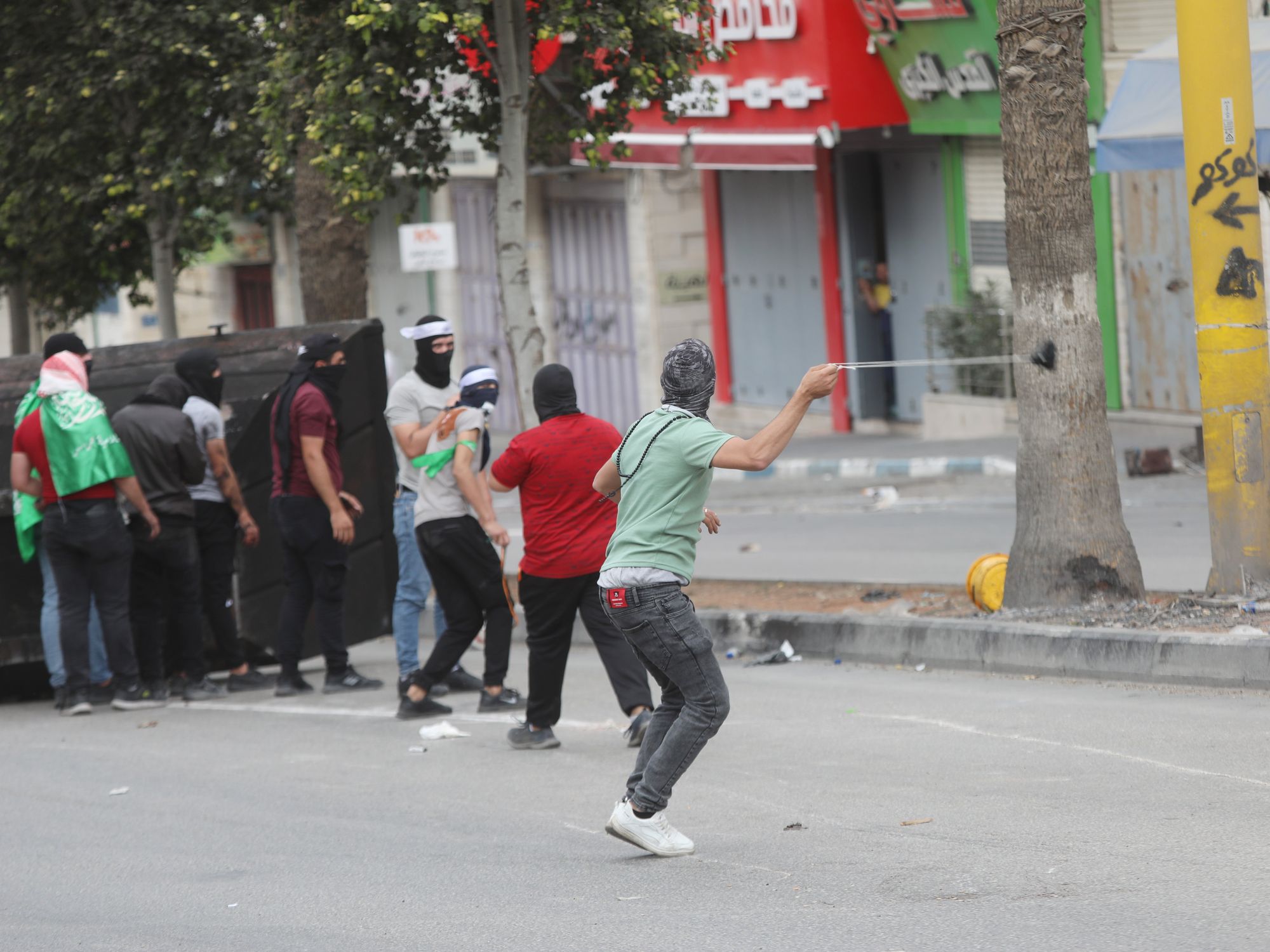 Photo of people Palestinians throwing stones toward Israeli troops