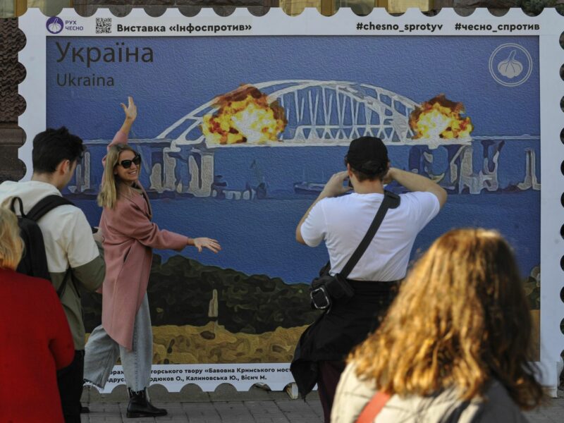 Photo of people taking pictures in front of an art installation in Kyiv showing the explosions on the Kerch bridge