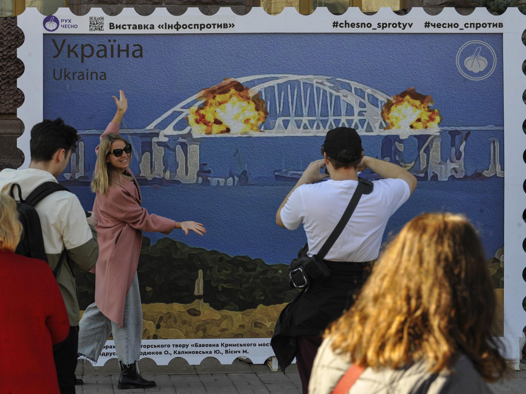 Photo of people taking pictures in front of an art installation in Kyiv showing the explosions on the Kerch bridge
