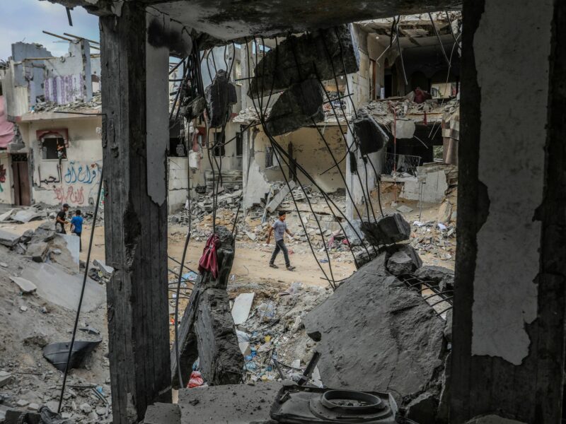 Photo of people walking by destroyed building in Rafah, Gaza