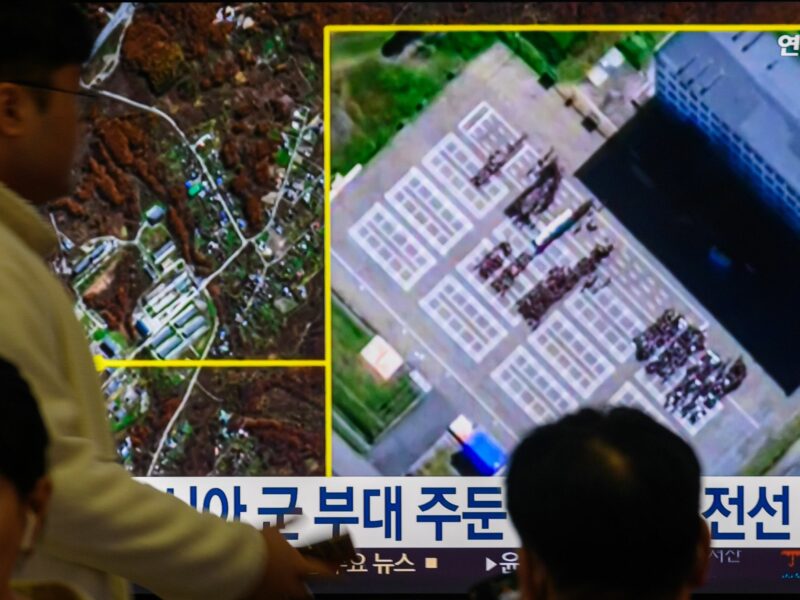 Photo of people walking past a TV showing a newscast of satellite footage of North Korean troops