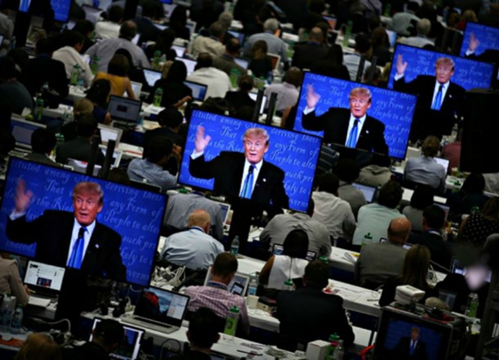 Photo of people working at desks with screens displaying images of Donald Trump